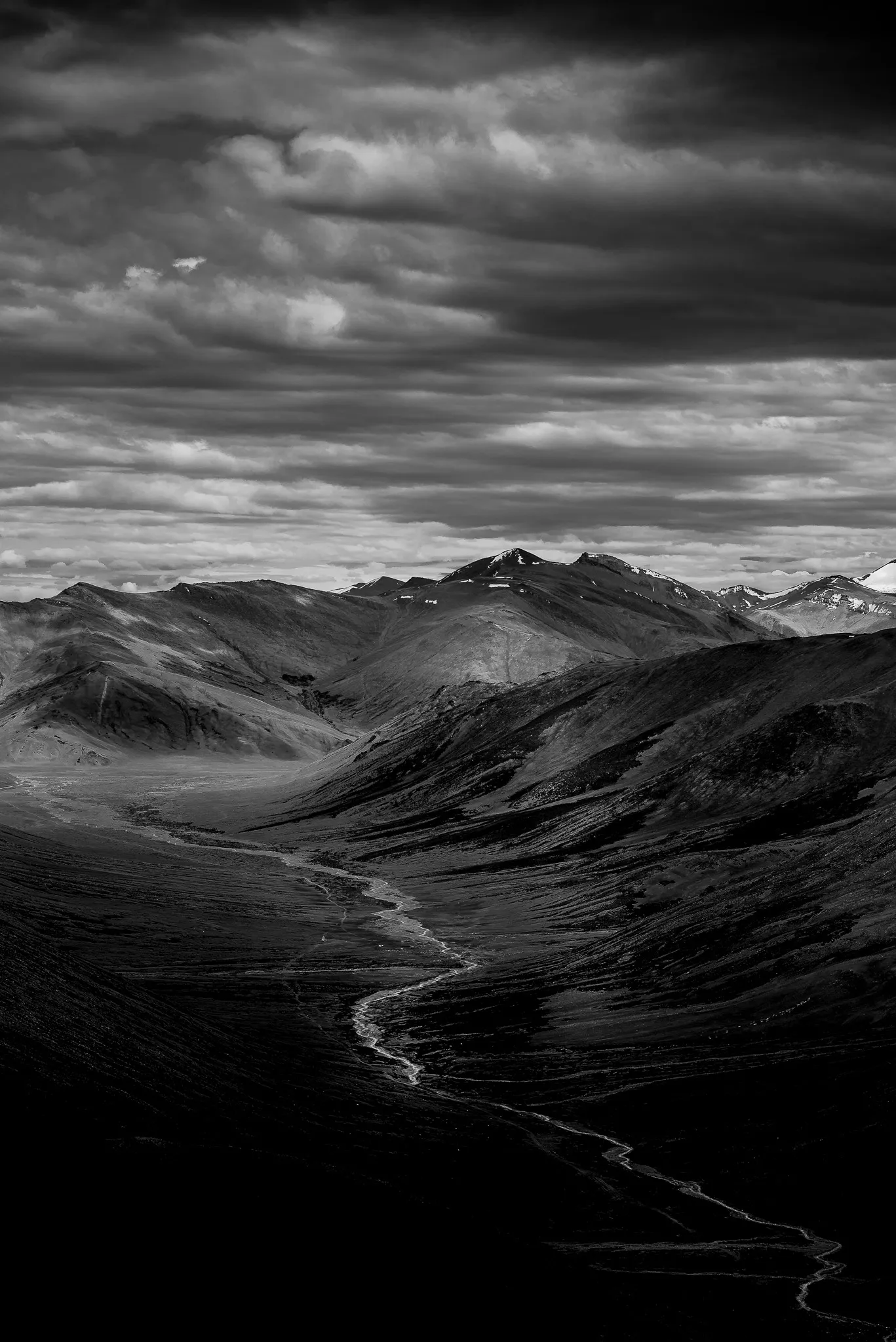 Black and white landscape of Ladakh mountains with a winding river through a vast valley under dramatic clouds