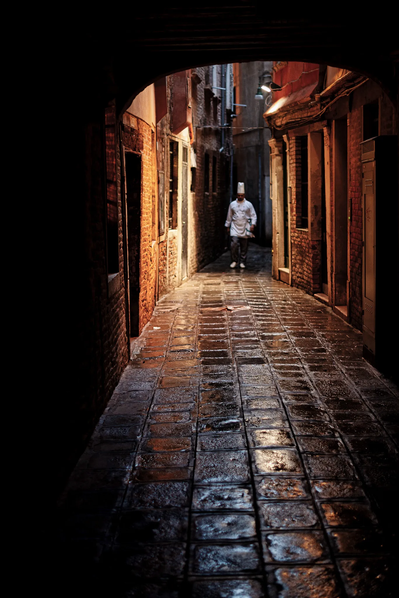 Dramatic night scene in Venice with red umbrella, reflections and lamplight on wet stone