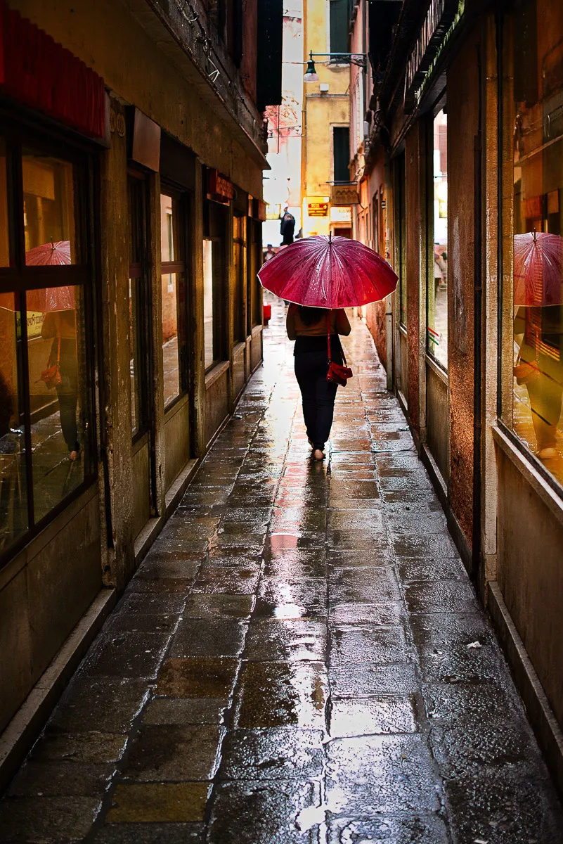 Red umbrella in a rain-soaked Venice alley
